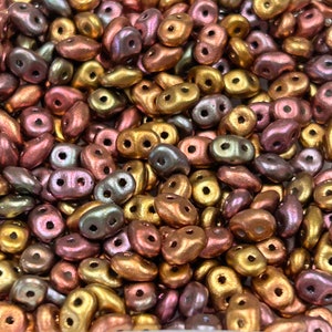 May include: A close-up of a pile of small, two-holed, iridescent glass beads in shades of gold, pink, and green.