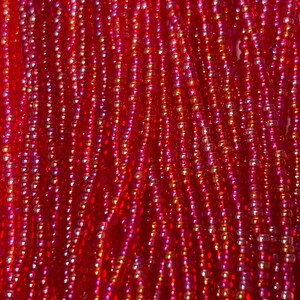 May include: Close-up of strands of red beads. The beads are small, round, and have a glossy finish. The color varies from a deep red to a lighter, almost pink hue, with hints of gold. The beads are strung together, creating a textured surface.