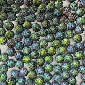 May include: A collection of iridescent glass beads in shades of green, blue, and purple. The beads have a textured surface and a round shape. These beads are suitable for jewelry making and other craft projects.