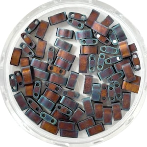 May include: A selection of rectangular beads in a clear, circular container. The beads have a metallic finish with bronze and teal hues. Each bead is designed with two holes for threading. These beads are suitable for jewellery making or other crafts.