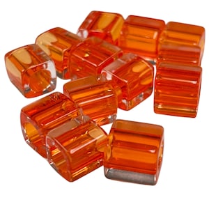 May include: A group of orange glass beads with a square shape and a hole in the center. The beads are translucent and have a slightly frosted finish.