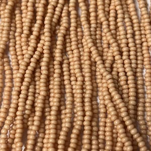 May include: Close-up of strands of small, round, light peach-colored beads. The beads are strung together, creating a textured surface. The beads are uniform in size and shape, and the color is consistent throughout.