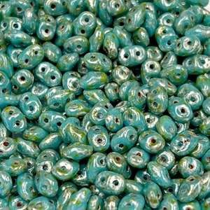 May include: A close-up of a pile of turquoise blue glass beads with silver accents. The beads are shaped like teardrops with two holes.