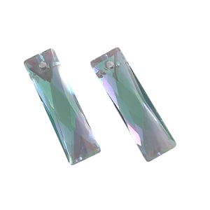 May include: Two iridescent crystal pendants with rectangular shapes. Each pendant has a small hole at the top for stringing. The crystals reflect shades of green, blue, and purple, creating a shimmering effect. The pendants are set against a white background.