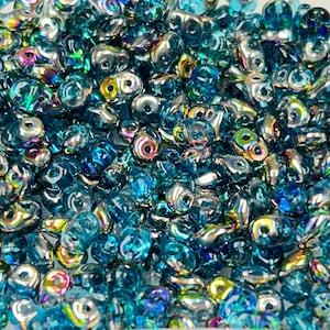 May include: A close-up of a pile of iridescent blue glass beads. The beads are shaped like teardrops and have a metallic sheen.