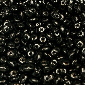 May include: A close-up image of a large quantity of black seed beads. The beads are small and have a slightly elongated, teardrop shape.