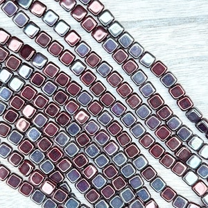 May include: A strand of square-shaped glass beads with a deep purple and iridescent finish. The beads are arranged in rows and have a slightly textured surface.