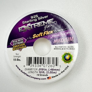 May include: A spool of 925 Sterling Silver Extreme Flex Soft Flex Company Plated Flex Wire in Medium size. The spool is white with purple and black text. The text reads "925 Sterling Silver Extreme Flex by Soft Flex Company Plated Flex Wire Medium". The spool also has a barcode and the text "Now with Extreme Abrasion Resistance, Test Strength 15 lbs., Diameter .019 in. (.48mm), Length 10 ft. (3.05m), 19 Strands, www.SoftFlexCompany.com, Made in the USA".