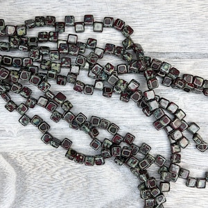 May include: A strand of dark red and green square beads with white speckles. The beads are made of glass and have a speckled finish.