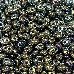 May include: A close-up view of a large quantity of small, dark brown, iridescent glass beads. The beads are oval shaped with two holes in each bead.