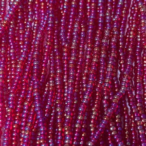 May include: Close-up of strands of small, round, iridescent beads in shades of red, pink, and gold. The beads are strung together, creating a textured, shimmering surface. The beads are likely used for jewelry making or other craft projects.