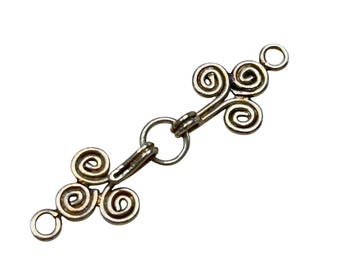May include: Silver-toned metal clasp with a decorative design of three interlocking spirals on each end. The clasp has two open loops for attaching to a necklace or bracelet.