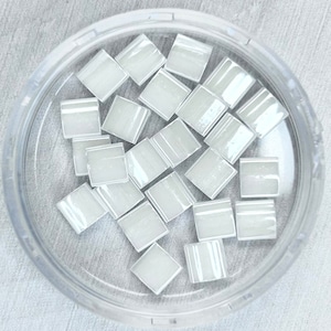 May include: A container of small, white, square tiles. The tiles are glossy and have a slight iridescent sheen.