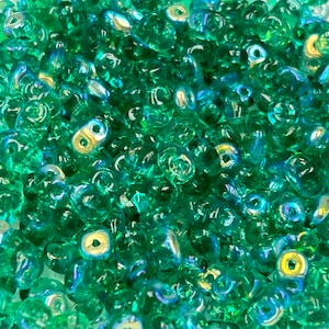 May include: A close-up of a large quantity of small, iridescent green glass beads. The beads are shaped like a teardrop with a small hole at the top.