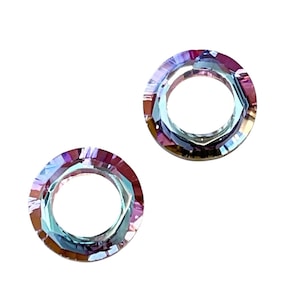 May include: Two iridescent crystal ring-shaped beads. The beads have a circular hole in the center and are faceted, reflecting light with a rainbow of colors, including pink, purple, and blue. The background is white.