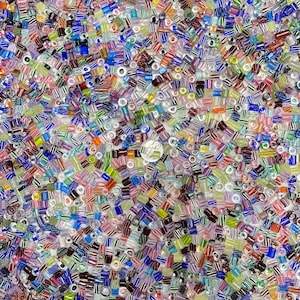 May include: A vibrant assortment of small glass beads in various shapes and colors, including blue, green, pink, and white. Some beads have striped patterns. A silver coin is visible among the beads.