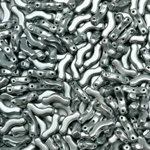 May include: A close-up shot of a pile of silver-colored metal beads. The beads have a curved, elongated shape with multiple holes for stringing. The beads are scattered, creating a textured surface.