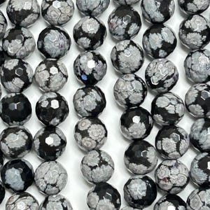 May include: A strand of black and white snowflake obsidian beads. The beads are faceted and have a speckled pattern.