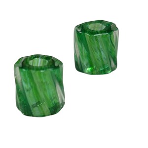 May include: Two green glass candle holders with a spiral design. The holders are cylindrical with a hollow center. The glass has a translucent quality, allowing light to pass through. The color is a vibrant, emerald green.