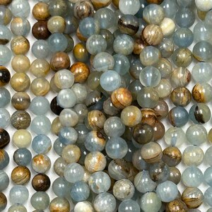 May include: A collection of round gemstone beads in various shades of blue, brown, and tan. The beads are smooth and polished, with a mix of opaque and translucent textures. The beads are likely for jewelry making or other craft projects.
