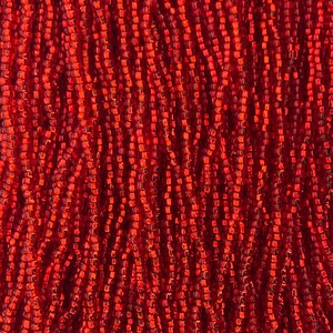 May include: Close-up of a mass of small, red beads. The beads are rectangular and strung together, creating a textured, flowing appearance. The color is a vibrant, deep red with subtle variations in tone, suggesting a handmade quality. Ideal for jewelry making.