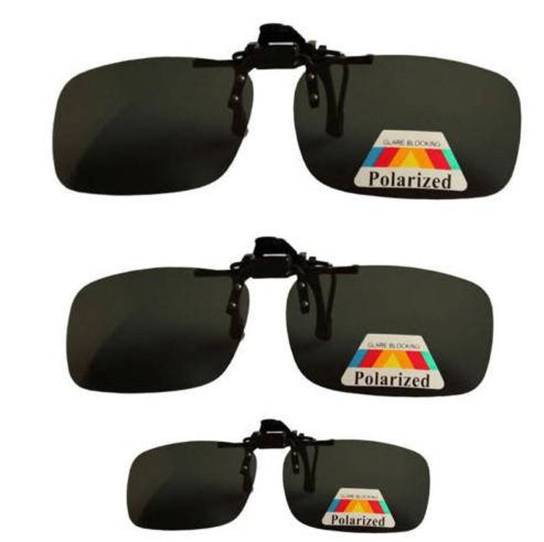 Puede incluir: Tres pares de gafas de sol clip-on negras con lentes polarizadas. Las lentes son de color gris oscuro y las monturas son negras. Las gafas de sol tienen un clip de resorte que se fija al puente de las gafas.