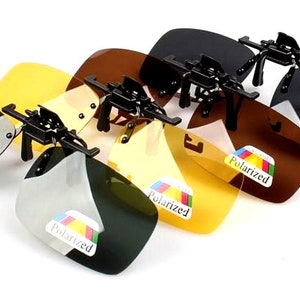 Puede incluir: Cuatro pares de gafas de sol polarizadas de clip en diferentes colores: negro, marr&oacute;n, amarillo y verde. Cada par tiene una montura negra y una etiqueta que dice "Polarizado".