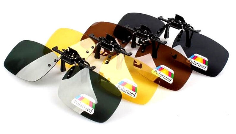 Puede incluir: Cuatro pares de gafas de sol polarizadas de clip en diferentes colores: negro, marr&oacute;n, amarillo y verde. Cada par tiene una montura negra y una etiqueta que dice "Polarizado".