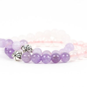 May include: Two bracelets made of amethyst and rose quartz beads. The amethyst bracelet has silver flower-shaped beads.