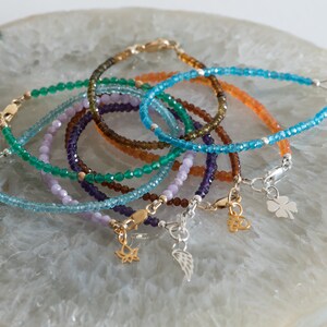 Peut inclure: Un ensemble de sept bracelets en pierres pr&eacute;cieuses avec des breloques en argent et en or. Les bracelets sont faits de pierres pr&eacute;cieuses de diff&eacute;rentes couleurs, notamment le vert, le bleu, le violet et le brun. Les breloques comprennent une plume, une fleur de lotus et un tr&egrave;fle &agrave; quatre feuilles.