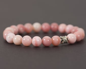 Könnte beinhalten: Ein Armband aus rosa Opalperlen mit einem silbernen Anhänger. Das Armband besteht aus runden, glatten Perlen und hat ein schlichtes Design.