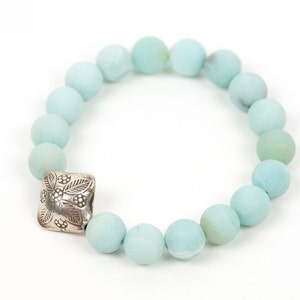 May include: A light blue beaded bracelet with a silver charm featuring a floral design.
