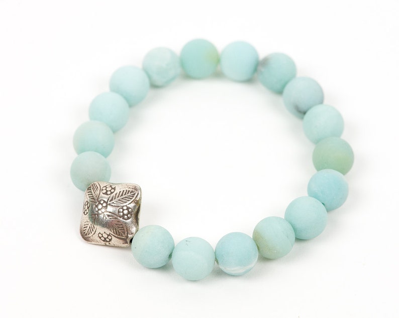 May include: A light blue beaded bracelet with a silver charm featuring a floral design.