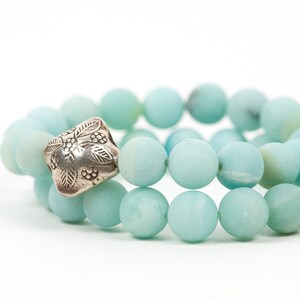 May include: A double-strand bracelet made of light blue gemstone beads with a silver charm featuring a floral design.