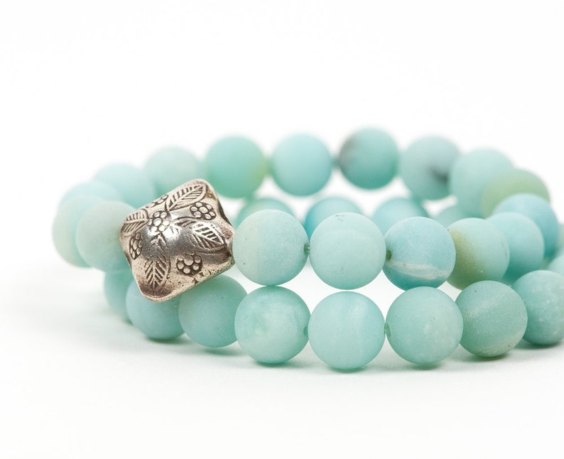 May include: A double-strand bracelet made of light blue gemstone beads with a silver charm featuring a floral design.