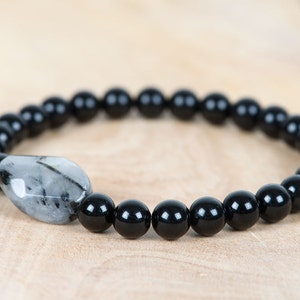 May include: A black beaded bracelet with a single, clear, faceted gemstone bead.