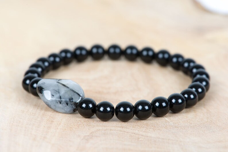 May include: A black beaded bracelet with a single, clear, faceted gemstone bead.
