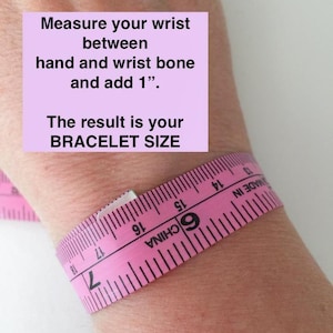 Peut inclure: Ruban &agrave; mesurer rose enroul&eacute; autour d'un poignet avec des instructions pour mesurer le poignet entre la main et l'os du poignet et ajouter 1 pouce. Le texte "The result is your BRACELET SIZE" est &eacute;galement inclus.