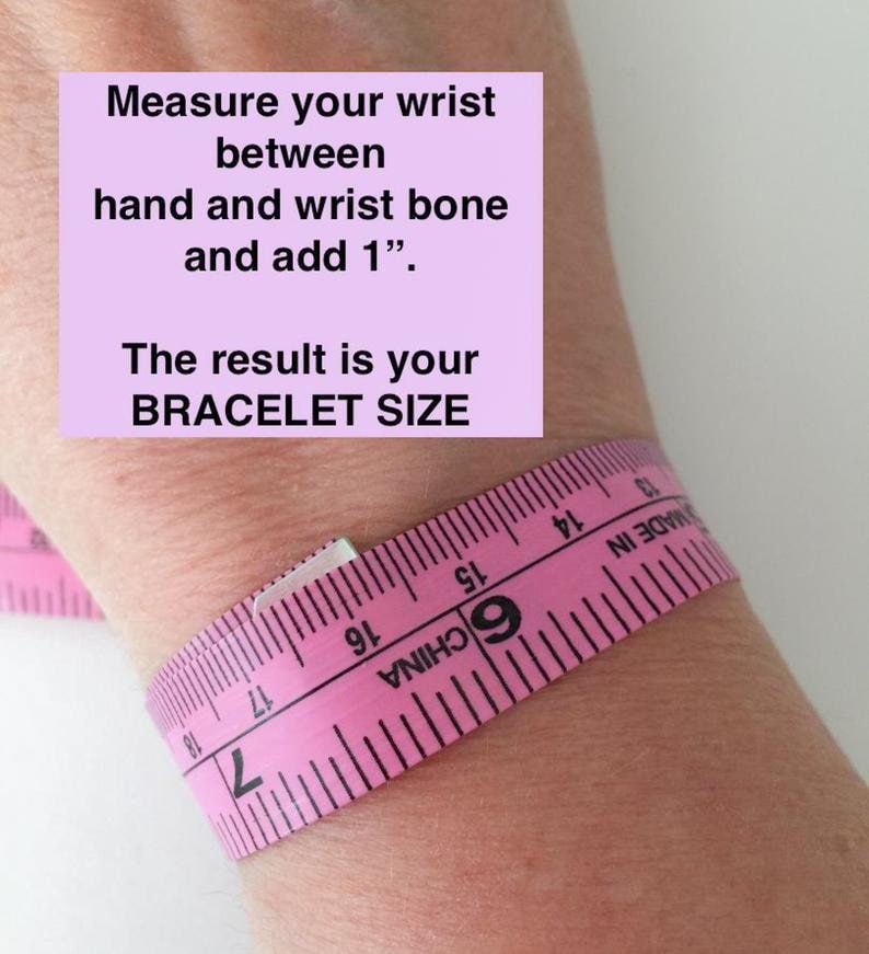 Peut inclure: Ruban &agrave; mesurer rose enroul&eacute; autour d'un poignet avec des instructions pour mesurer le poignet entre la main et l'os du poignet et ajouter 1 pouce. Le texte "The result is your BRACELET SIZE" est &eacute;galement inclus.