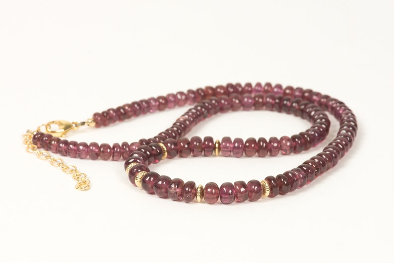 Puede incluir: Un collar hecho de peque&ntilde;as piedras preciosas redondas de color p&uacute;rpura con detalles dorados. El collar est&aacute; hecho de una cadena de cuentas con un cierre.