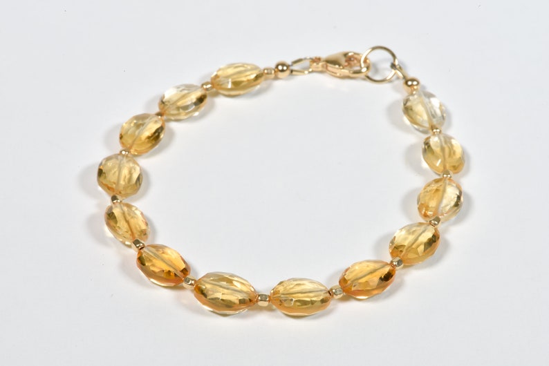May include: A gold bracelet with oval-shaped citrine gemstones. The bracelet has a lobster clasp closure.