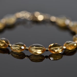 May include: A gold bracelet with oval-shaped, faceted, topaz gemstones. The bracelet is made of gold and has a clasp closure.