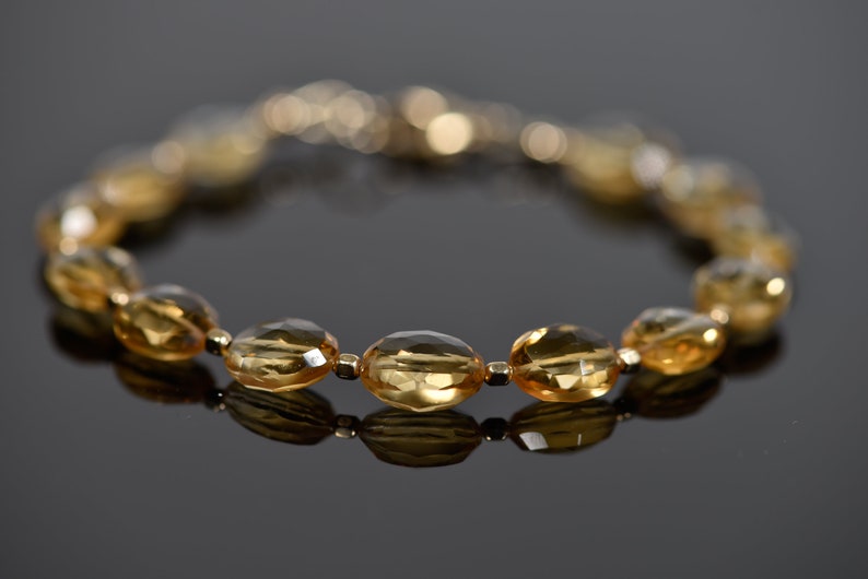 May include: A gold bracelet with oval-shaped, faceted, topaz gemstones. The bracelet is made of gold and has a clasp closure.