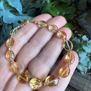May include: A gold bracelet with oval-shaped, translucent, yellow citrine gemstones. The bracelet is made with a gold clasp.