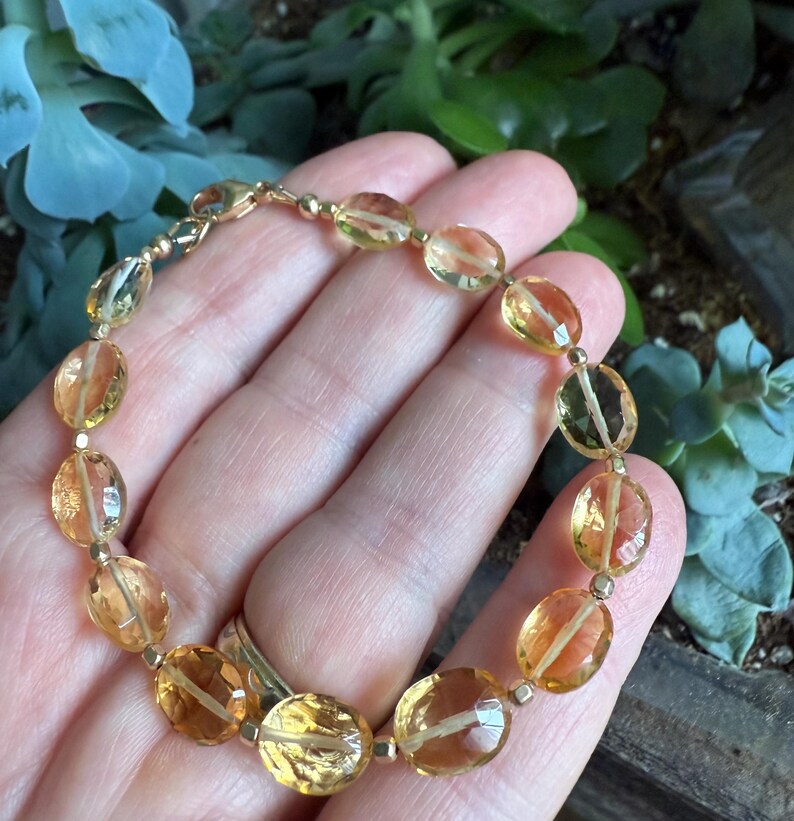 May include: A gold bracelet with oval-shaped, translucent, yellow citrine gemstones. The bracelet is made with a gold clasp.