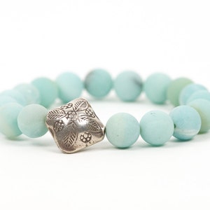 May include: A light blue beaded bracelet with a silver charm featuring a floral design.