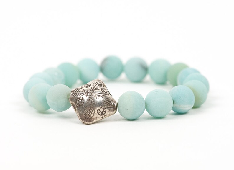 May include: A light blue beaded bracelet with a silver charm featuring a floral design.