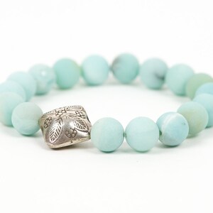 May include: A light blue beaded bracelet with a silver charm featuring a floral design.
