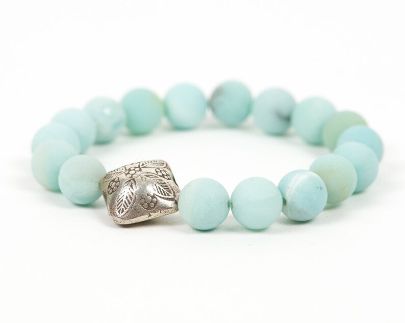 May include: A light blue beaded bracelet with a silver charm featuring a floral design.