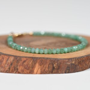 Op de afbeelding: Een groene edelsteen armband met een gouden sluiting. De armband is gemaakt van kleine, ronde kralen en wordt getoond op een houten oppervlak.
